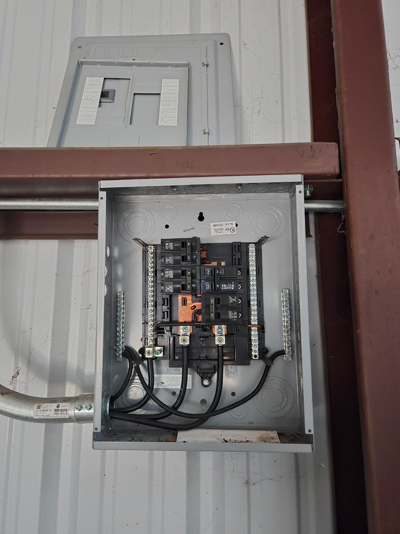 Open electrical panel with breakers and wiring mounted on a corrugated metal wall.