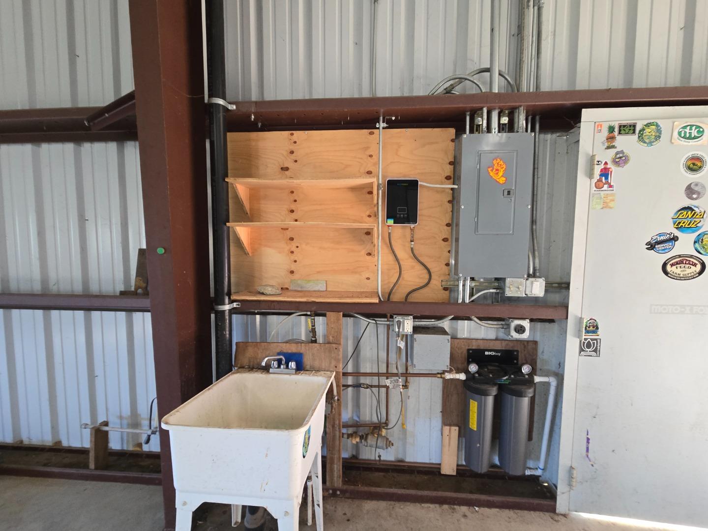 Utility area with an electrical panel, water filtration tanks, plywood shelving, and a large white sink.