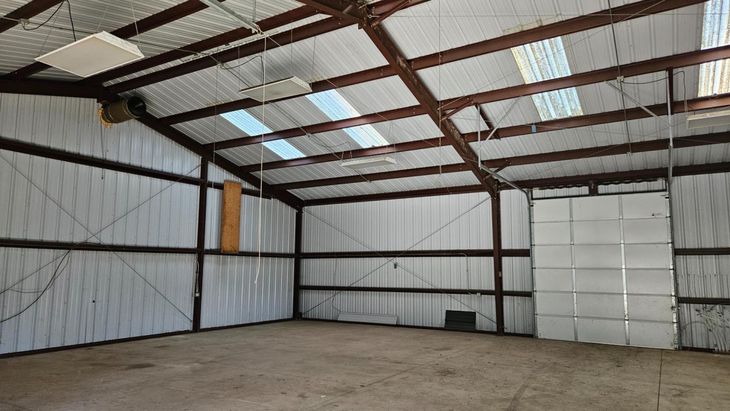 Large vacant metal building interior with exposed steel beams, skylights, and a tall garage door.