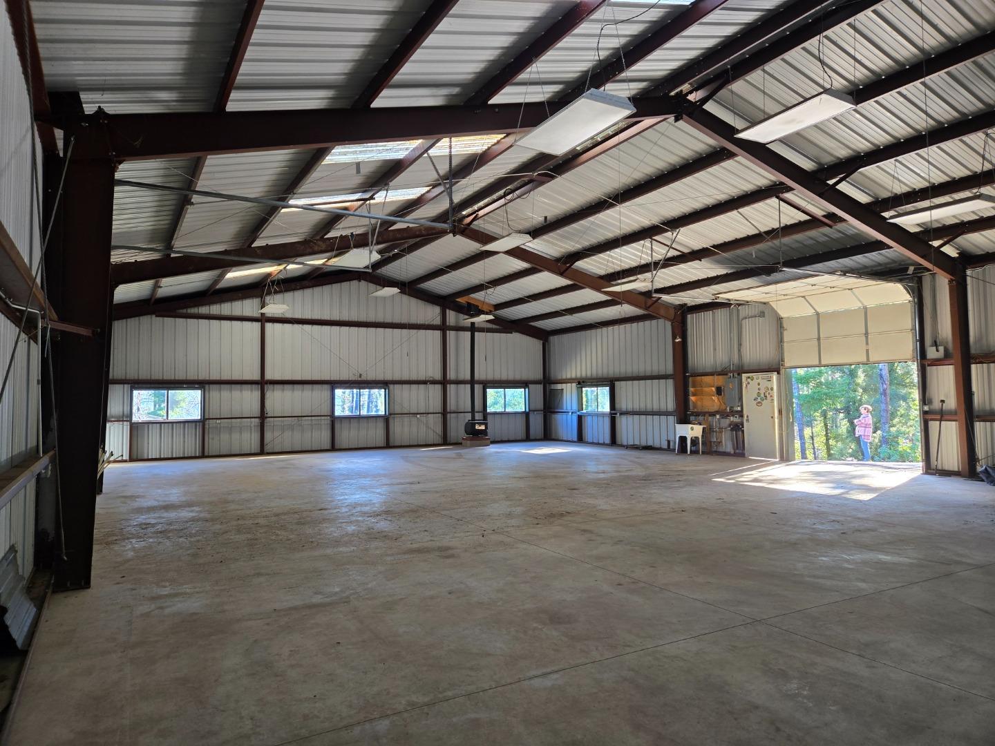 Empty metal workshop with exposed roof trusses, a broad concrete floor, and an open garage door.