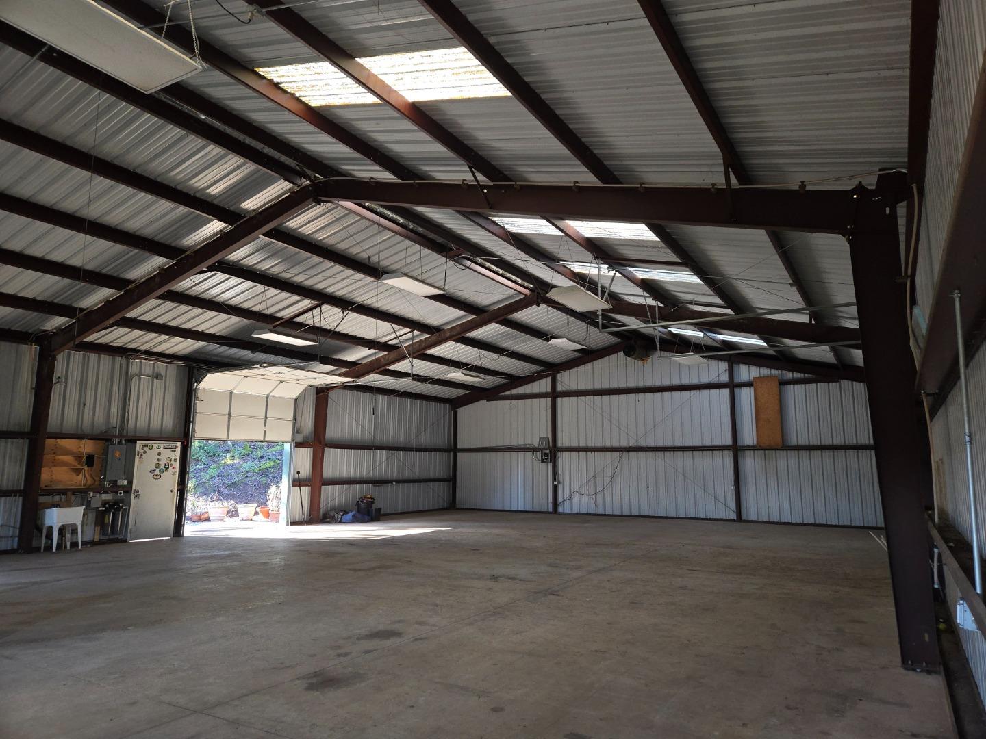 Large metal barn interior with exposed steel trusses, concrete floor, and open roll-up door.