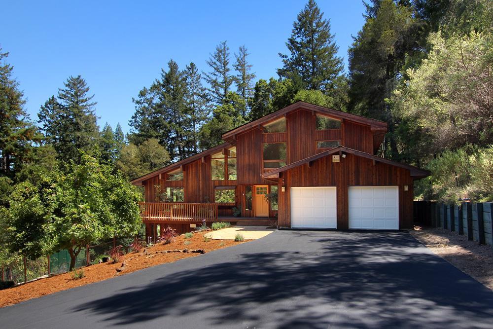 Multi-level wood-sided home with a two-car garage and broad driveway among tall trees.