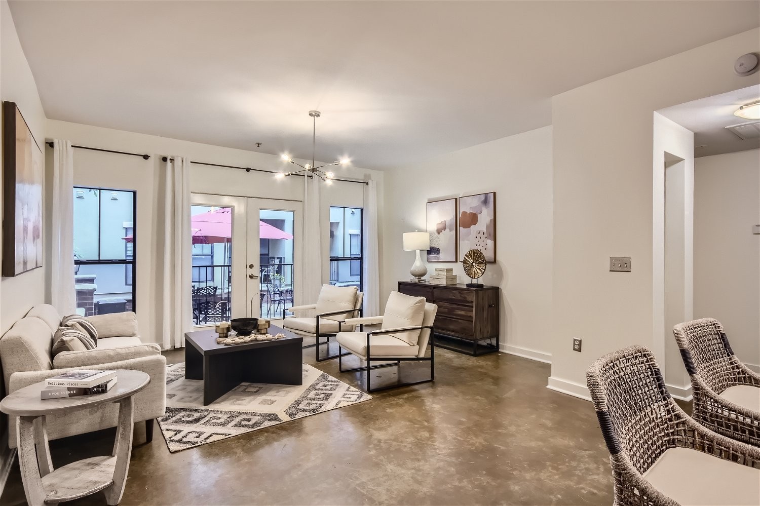Staged condo living room with cream seating, polished concrete floors, and balcony doors.