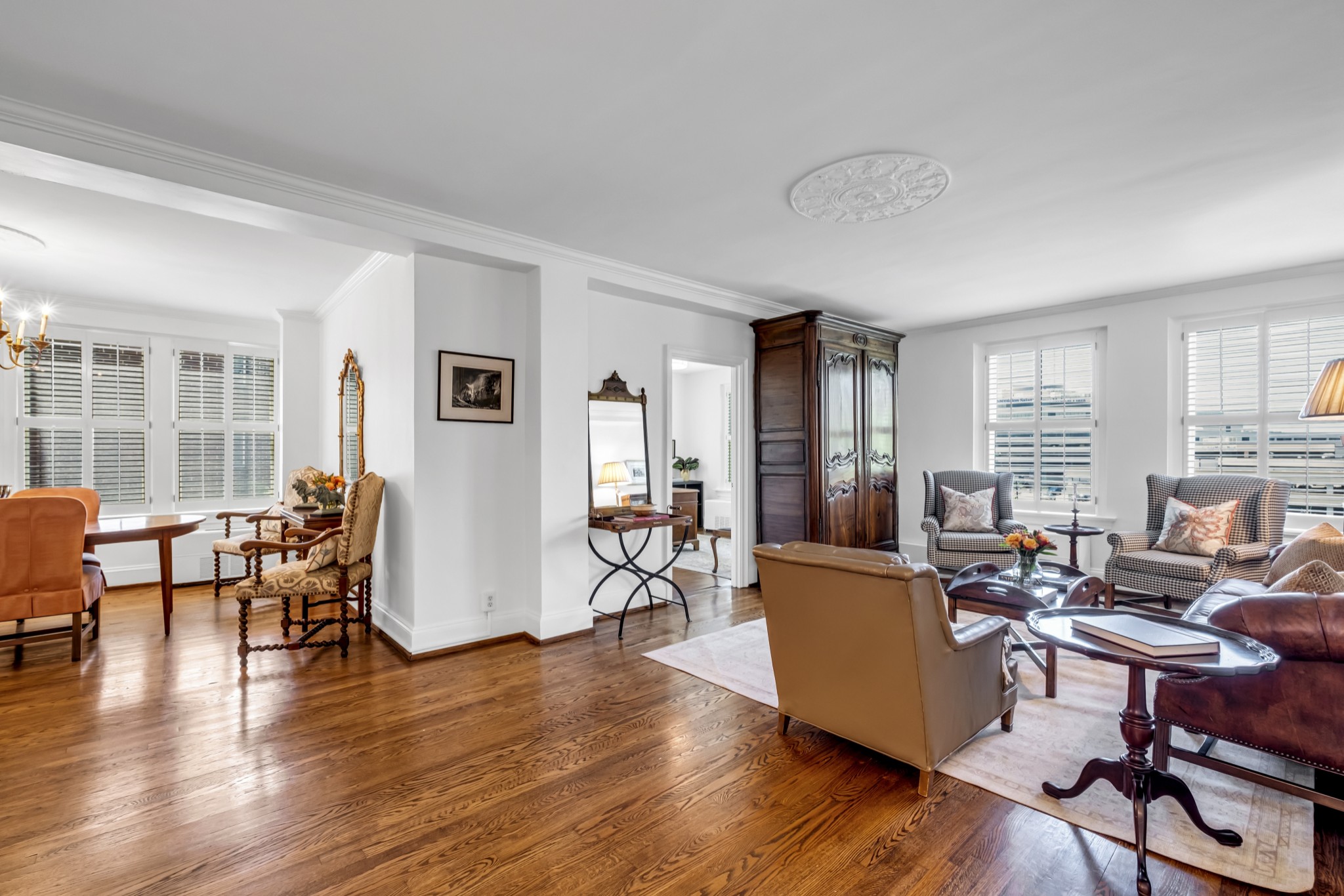 Living room with hardwood floors, shuttered windows, patterned armchairs, and an ornate wooden armoire.