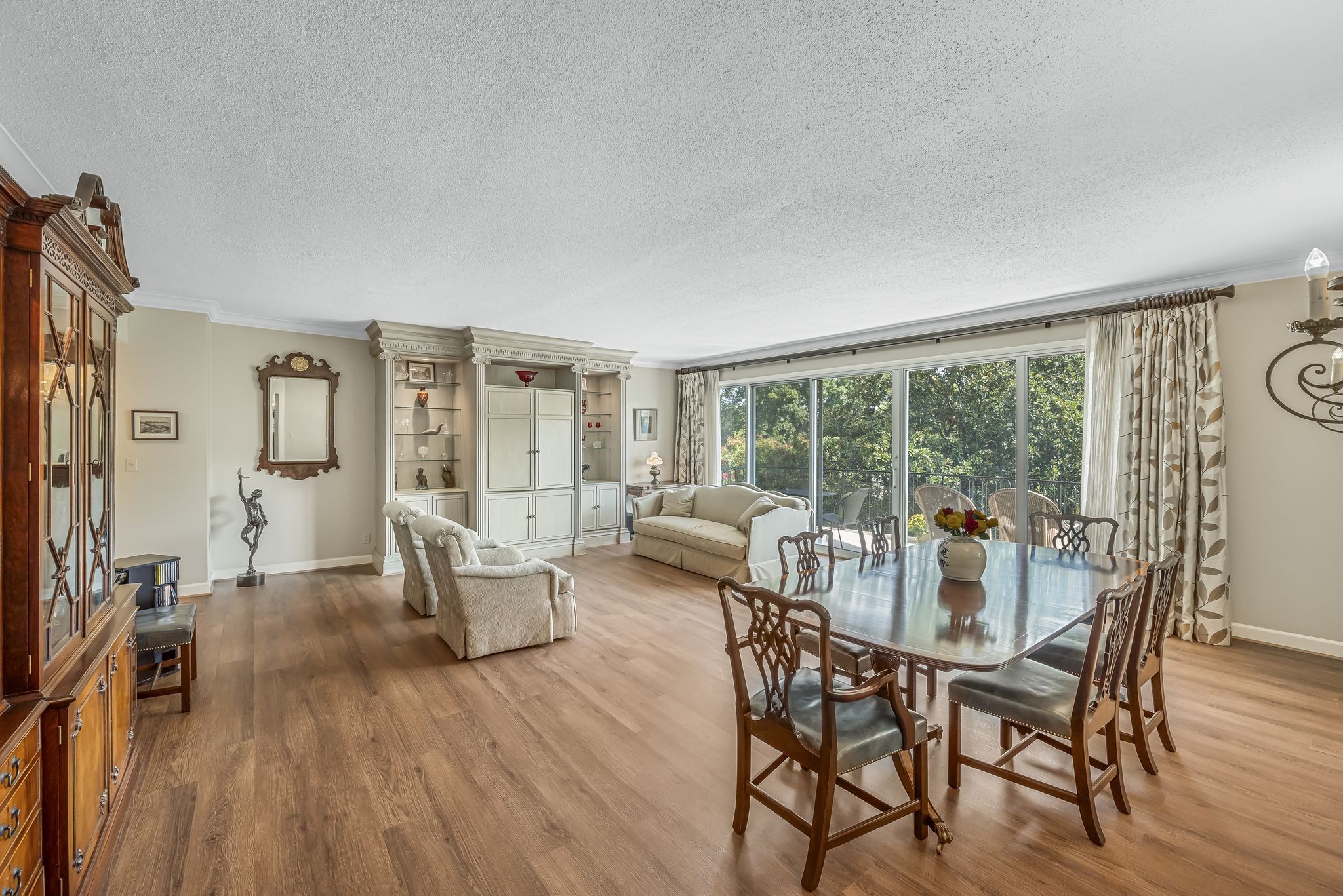 Open-plan living and dining room with built-in cabinetry and sliding doors to a leafy balcony.