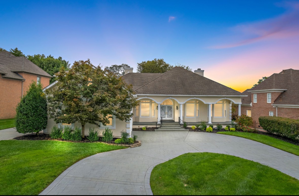Single-story home with an arched covered porch and curved driveway at dusk.