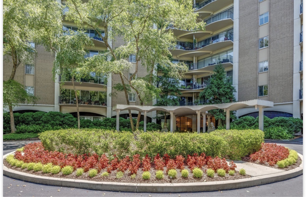 Multi-story condominium with curved balconies and colorful landscaping around its covered entrance.