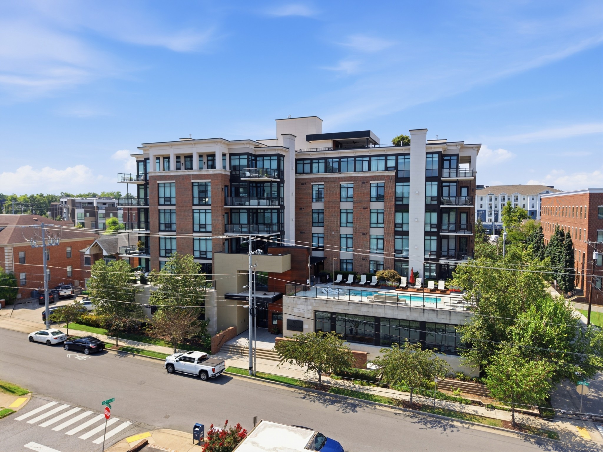 Modern brick and glass condominium building with balconies and a terrace swimming pool.