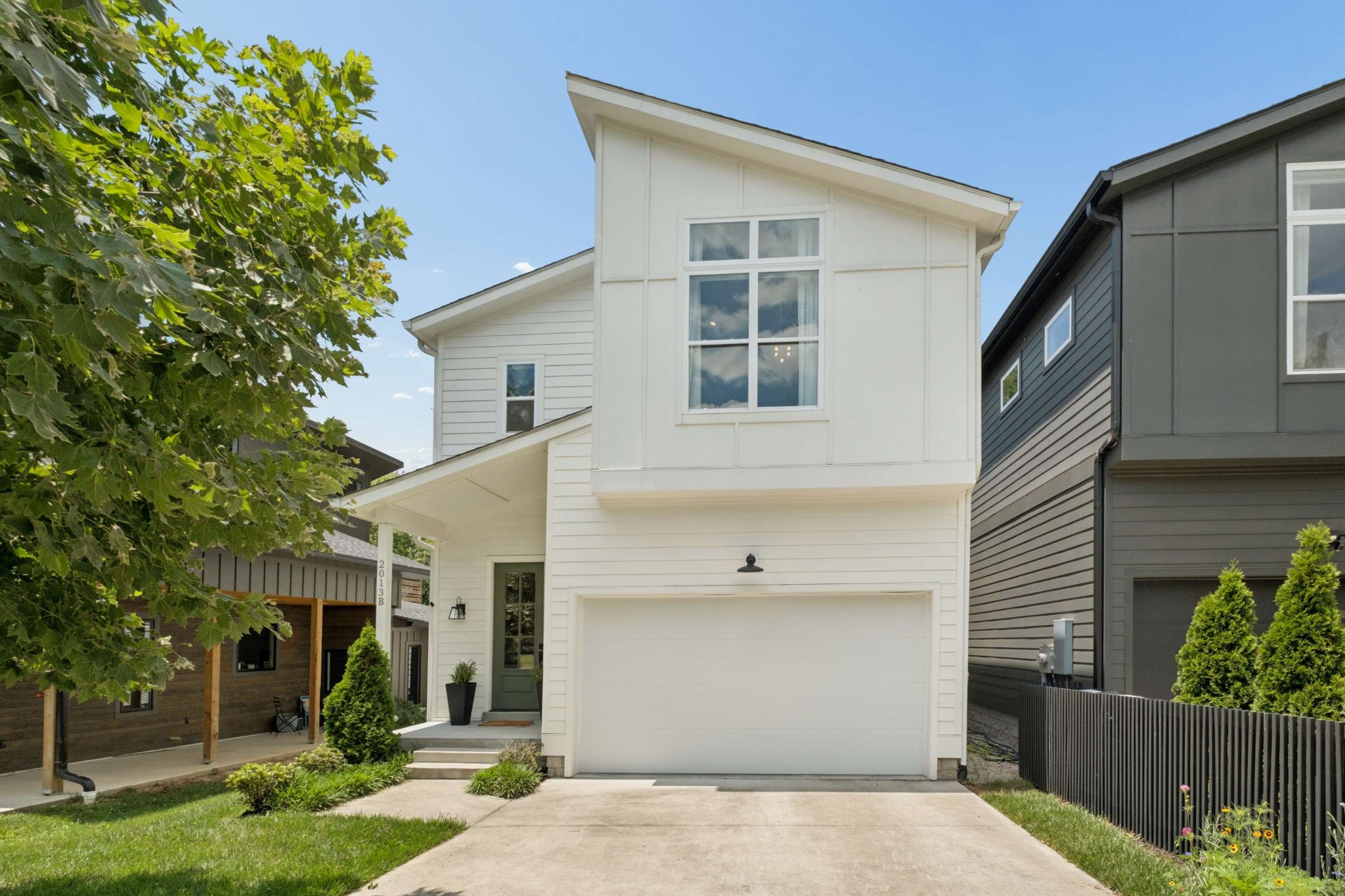 White two-story house with an attached garage, asymmetrical roofline, and leafy tree framing the front yard.
