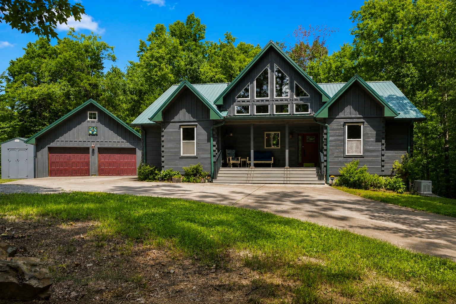 Dark gray gabled house with a green metal roof, double garage, and covered front porch.