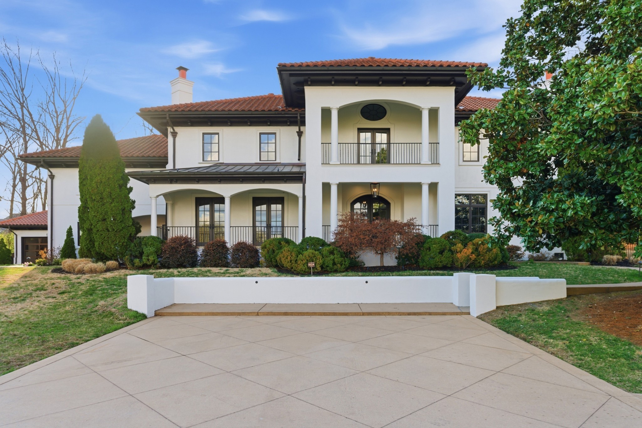 Large white house with red tile roofs, columned balconies, and a broad paved driveway.