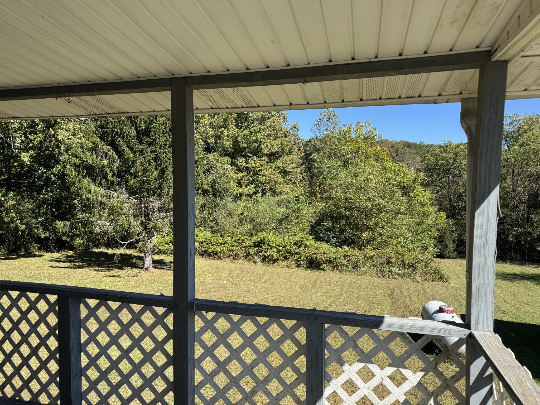 Covered porch overlooking a sunny lawn bordered by trees and shrubs.
