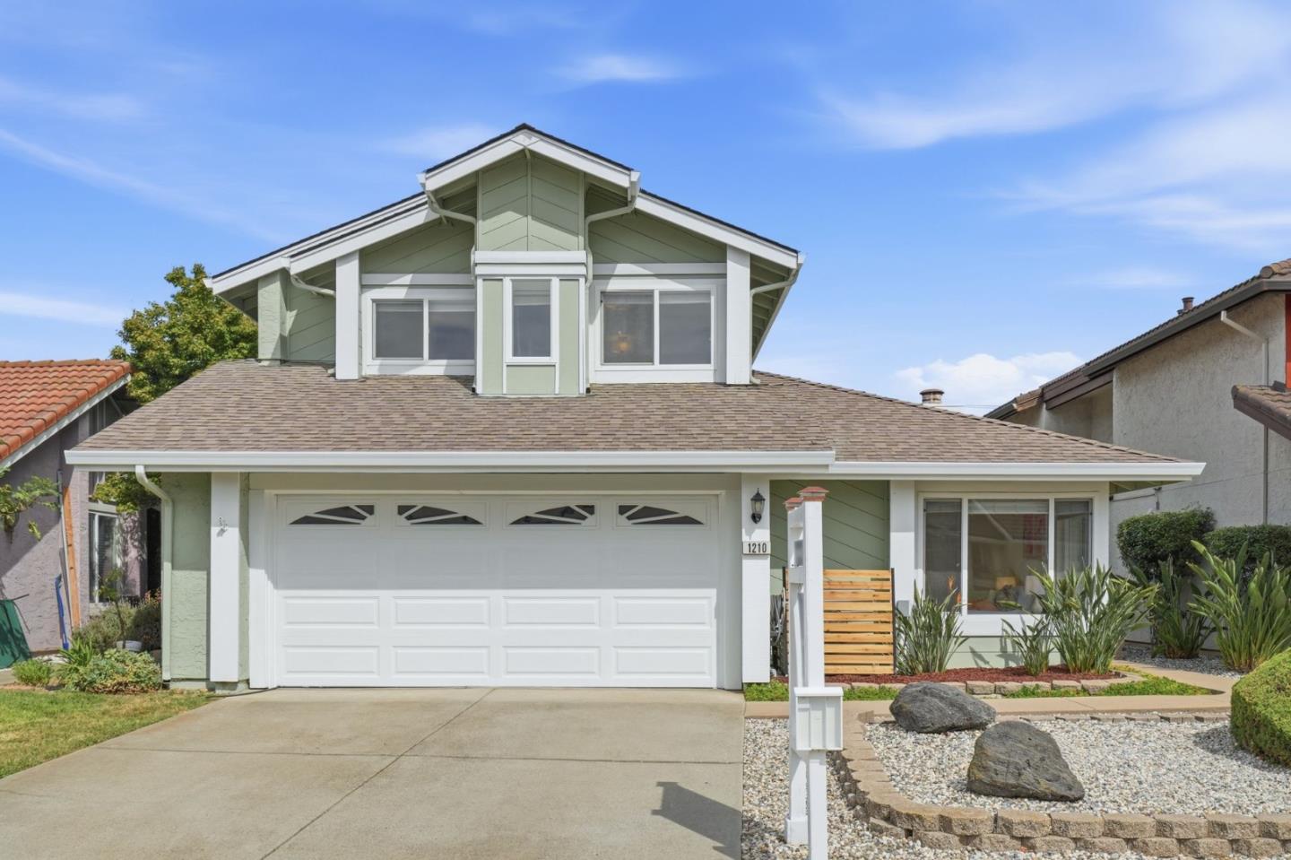 Pale green two-story home with white trim, a double garage, and a landscaped rock garden.