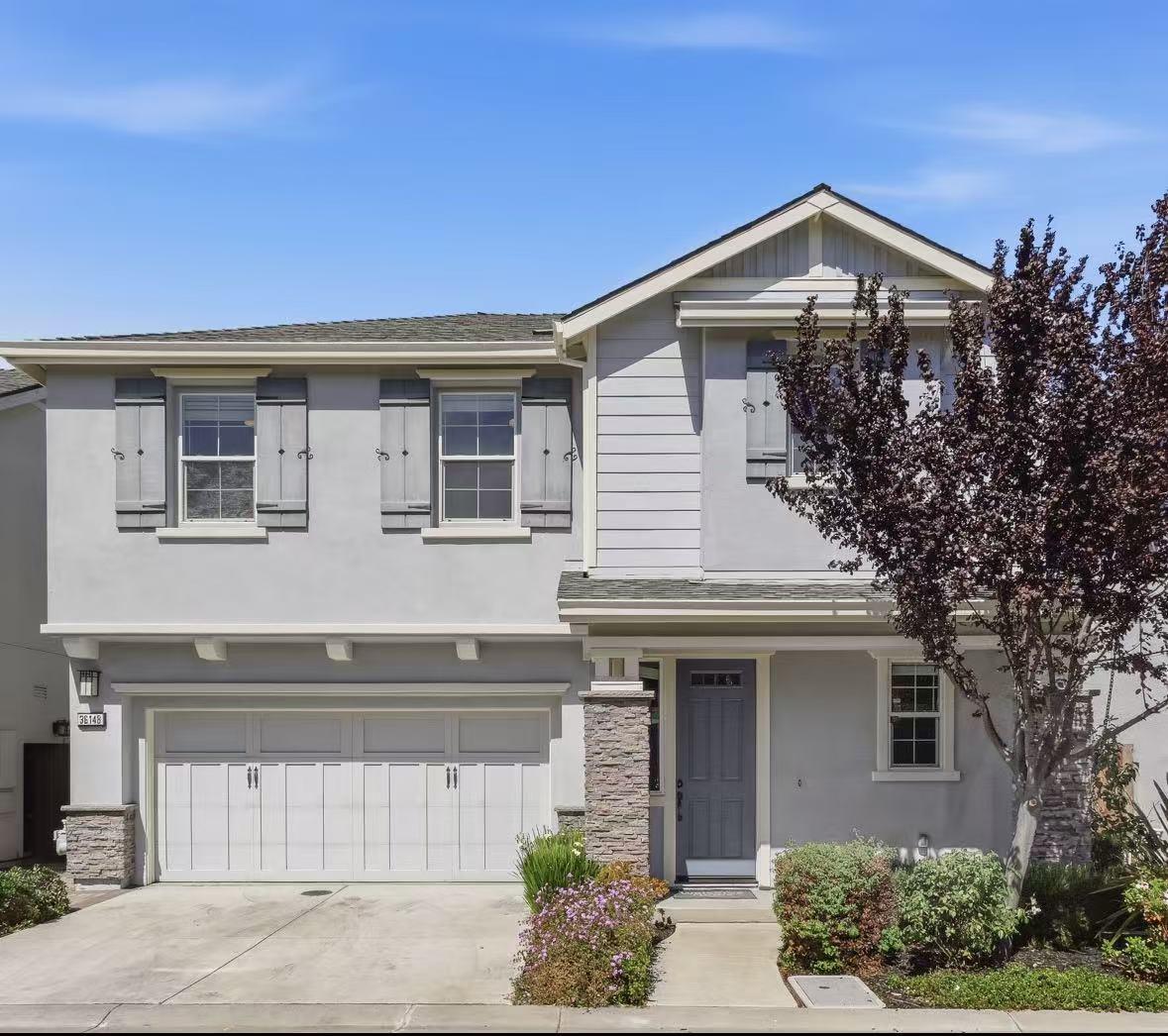 Two-story gray house with a blue front door, stone accents, and a broad two-car garage.