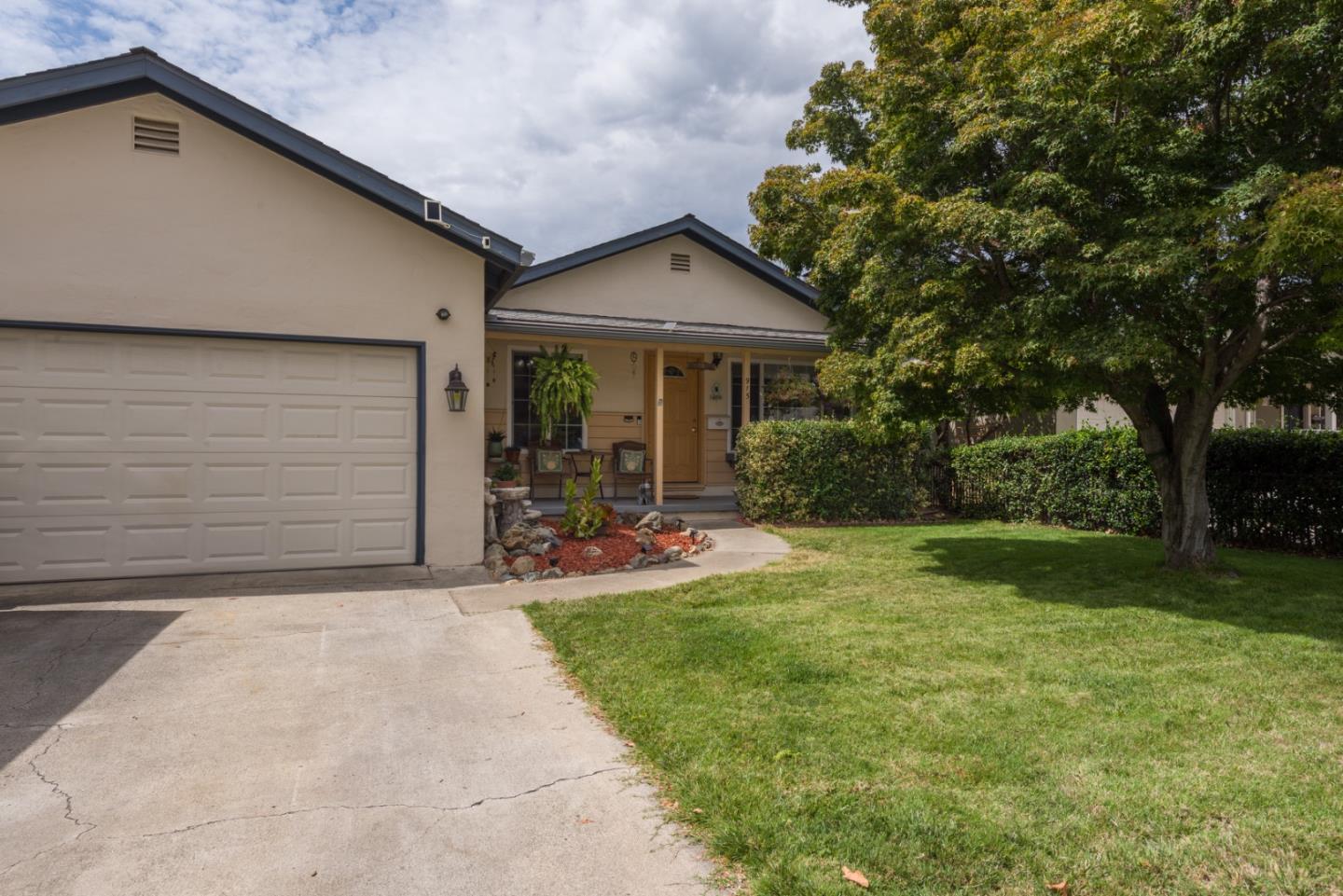 Single-story home with a two-car garage, covered porch, and large tree beside the front lawn.