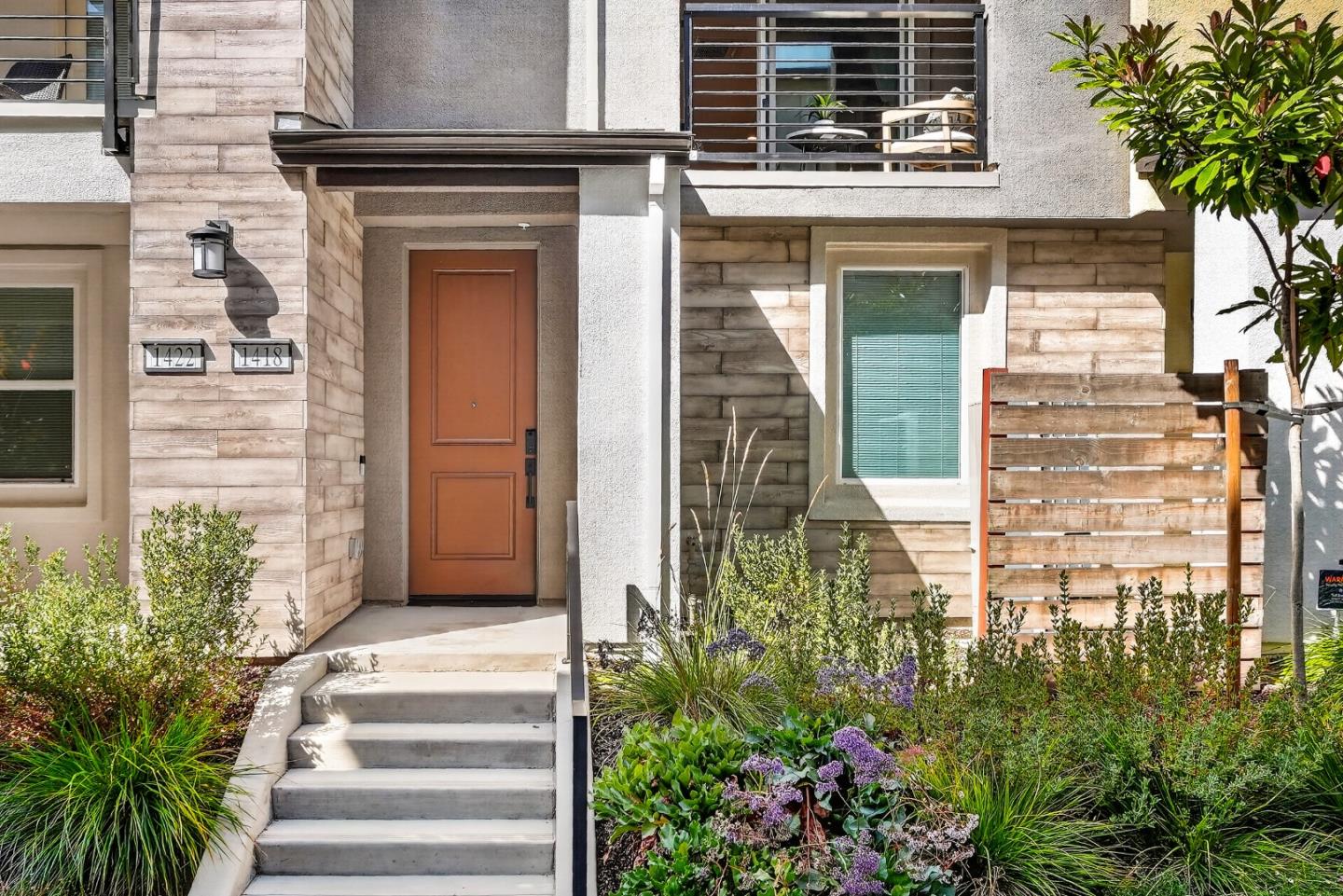 Townhouse entrance with terracotta door, concrete steps, stone-look cladding, and landscaped garden.