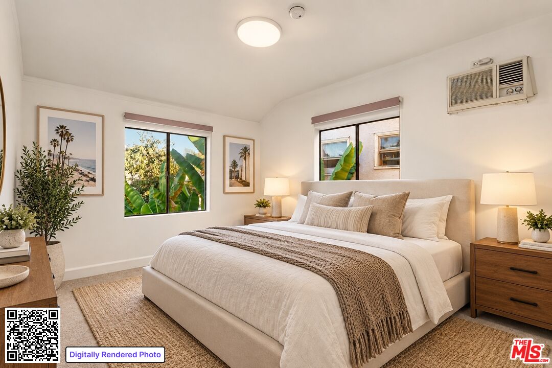 Bedroom with a large upholstered bed, neutral bedding, and leafy plants visible through the windows.