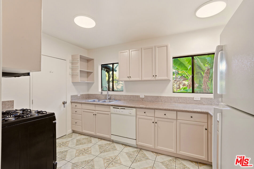 Kitchen with white cabinetry, long stone counters, geometric tile flooring, and windows facing tropical foliage.