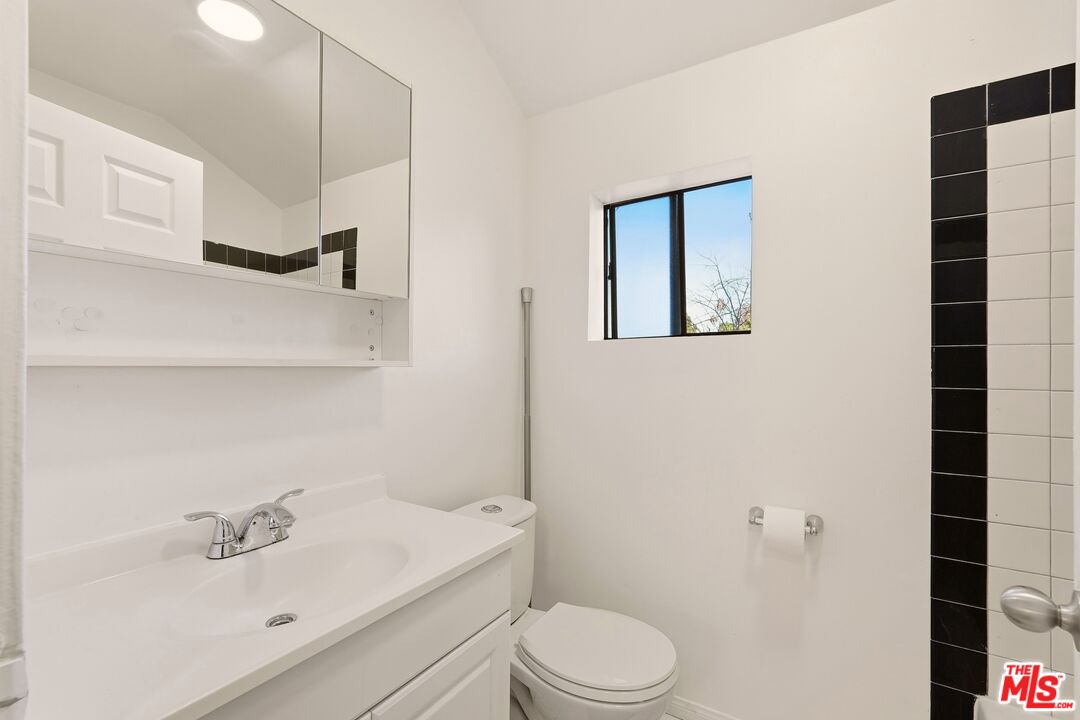 Bathroom with a white vanity, mirrored cabinet, toilet, and black-accented shower tiles.