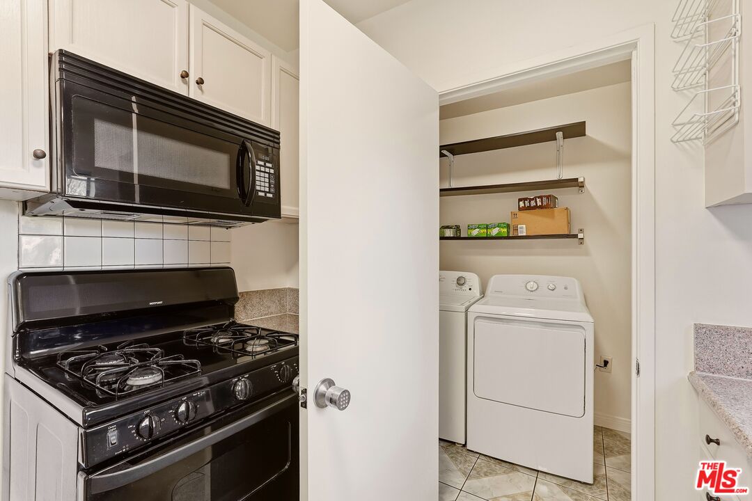 Kitchen with black gas range and microwave beside an open laundry closet with washer and dryer.