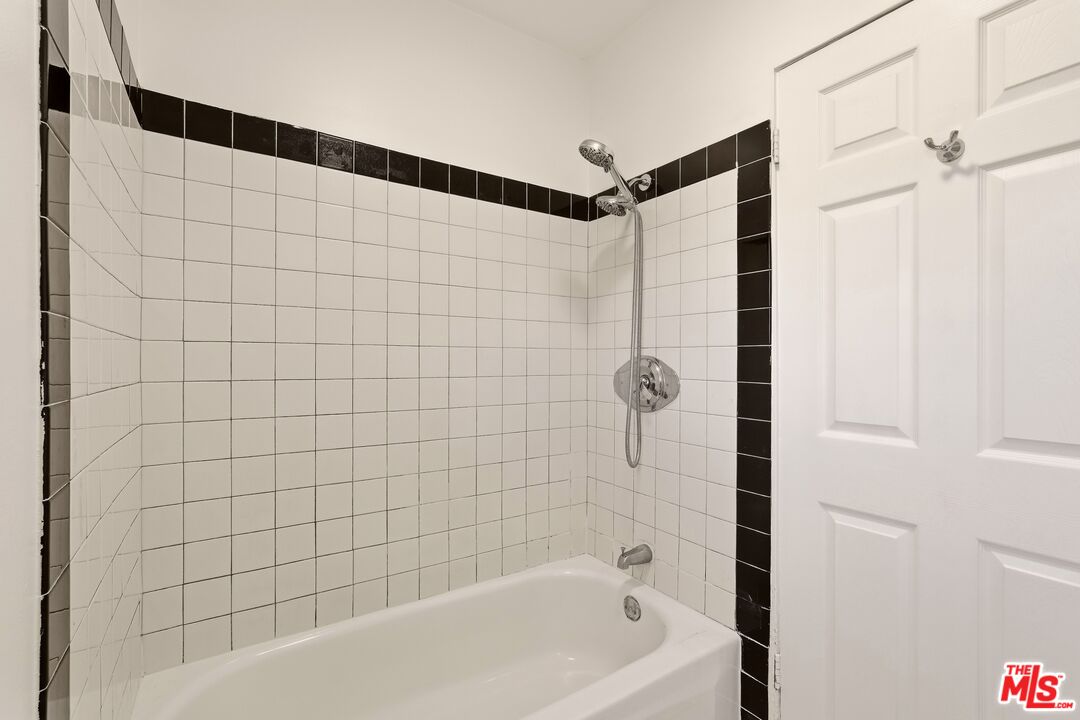Bathroom with a white tub, handheld showerhead, and white tile with black accents.