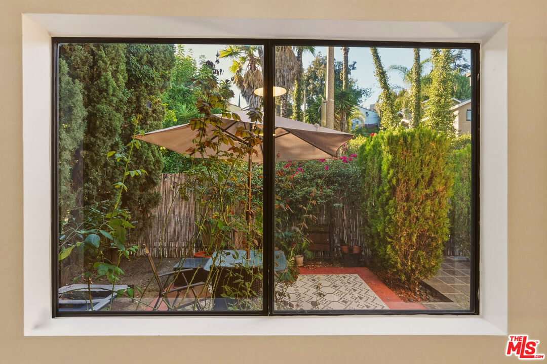 Window view of a secluded patio garden with an umbrella and dense greenery.