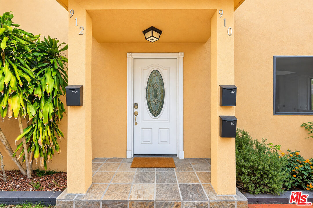 Home entrance with a white decorative glass door, tiled porch, and numbered mailboxes.