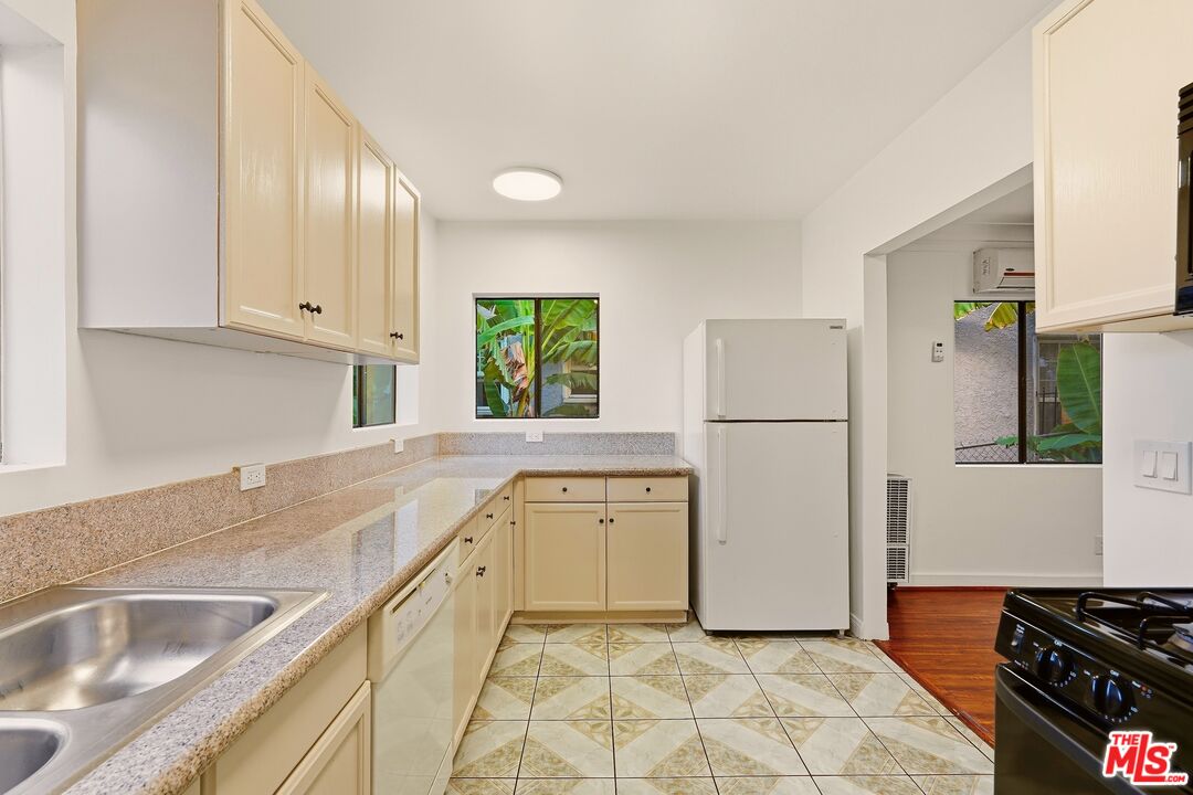 Galley kitchen with cream cabinets, patterned tile flooring, and windows overlooking tropical foliage.