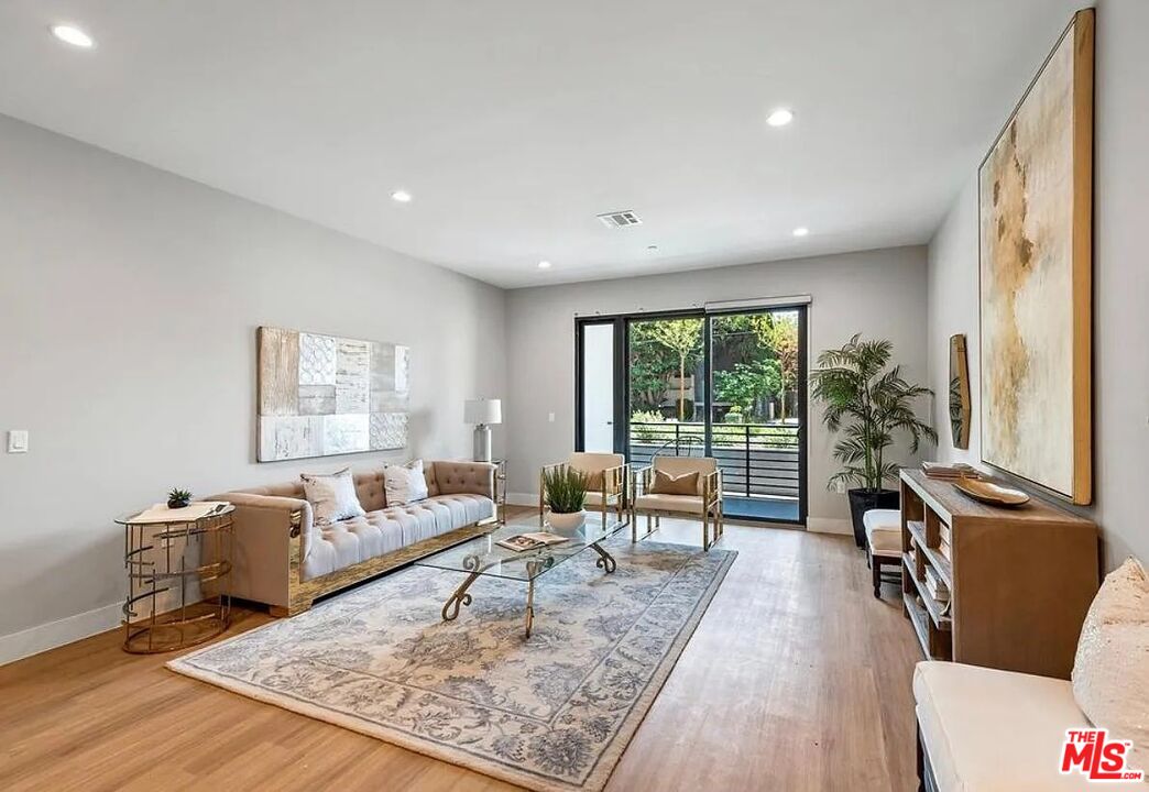 Living room with a neutral sofa, patterned rug, wood floors, and sliding doors to a balcony.
