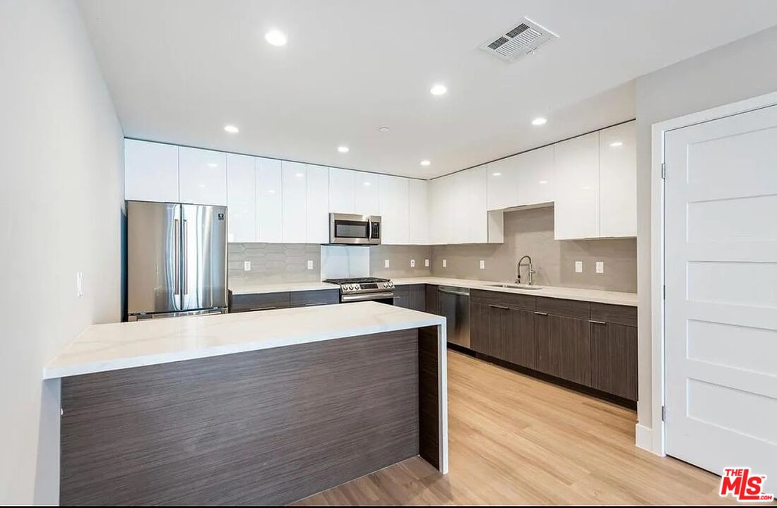Modern kitchen with a large peninsula, white upper cabinets, and stainless steel appliances.