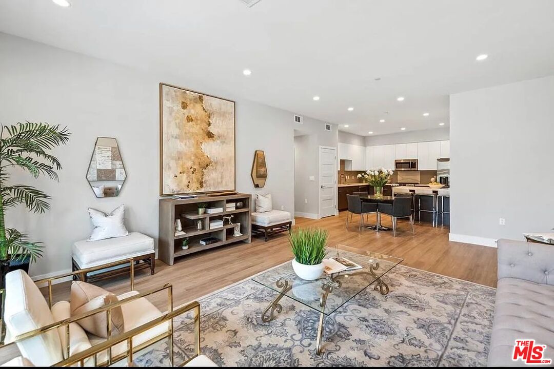 Furnished living room with a patterned rug, glass coffee table, and open kitchen.