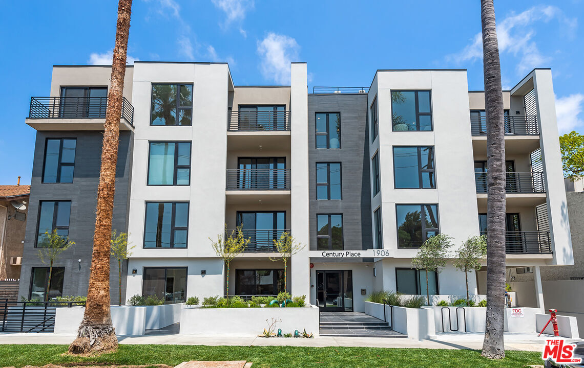 Modern apartment building with white and gray façades, balconies, and palm trees.