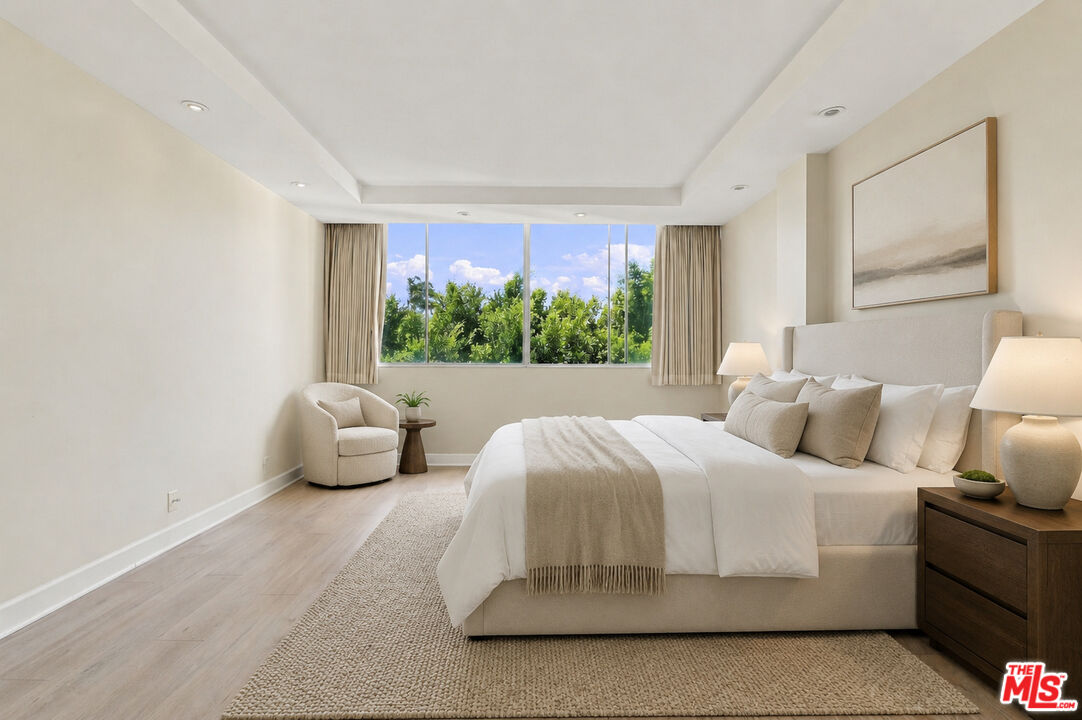 Neutral bedroom with an upholstered bed and a wide window overlooking leafy trees.