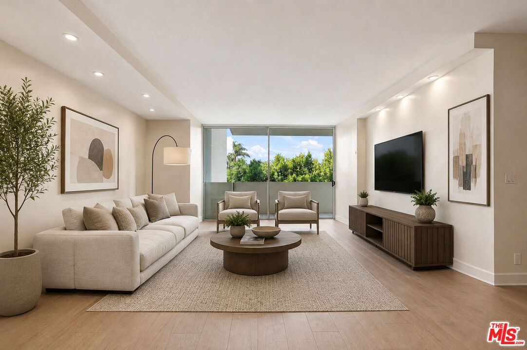 Living room with a cream sectional, round coffee table, and balcony doors overlooking trees.