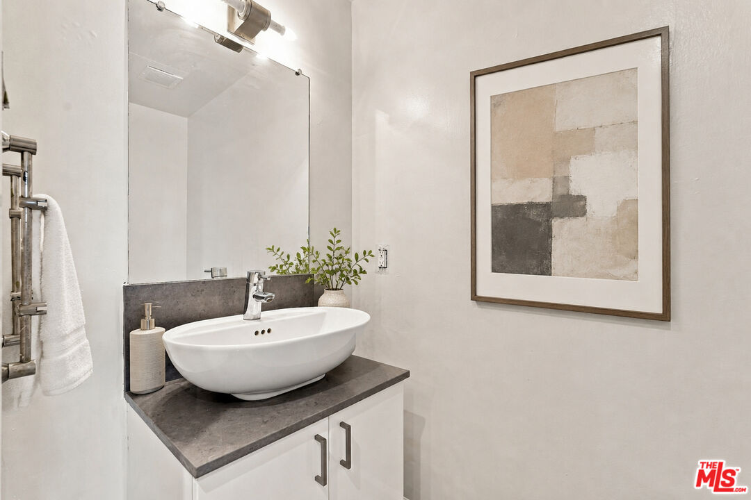 Bathroom vanity with a white vessel sink, dark stone counter, large mirror, and framed abstract artwork.