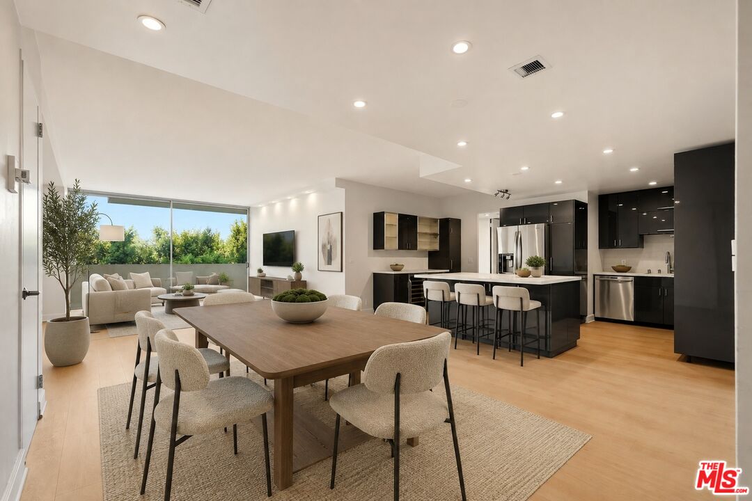 Open-plan dining room and kitchen with dark cabinetry, a wood table, and wide garden-facing windows.