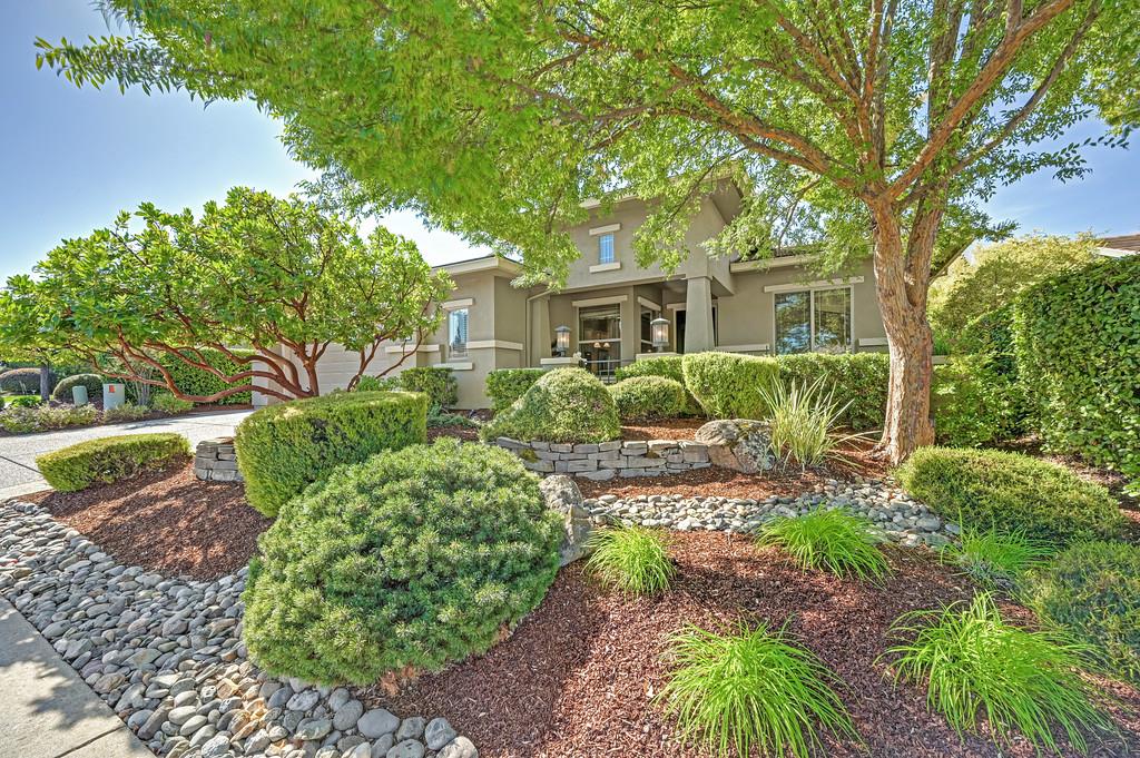Two-story gray stucco home framed by mature trees and landscaped gardens.