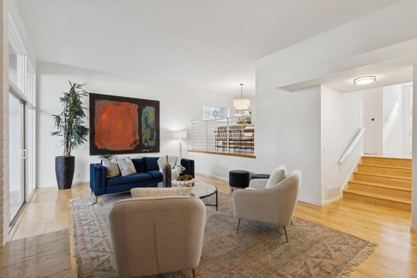 Bright living room with a navy sofa, large abstract painting, sliding glass doors, and wood staircase.