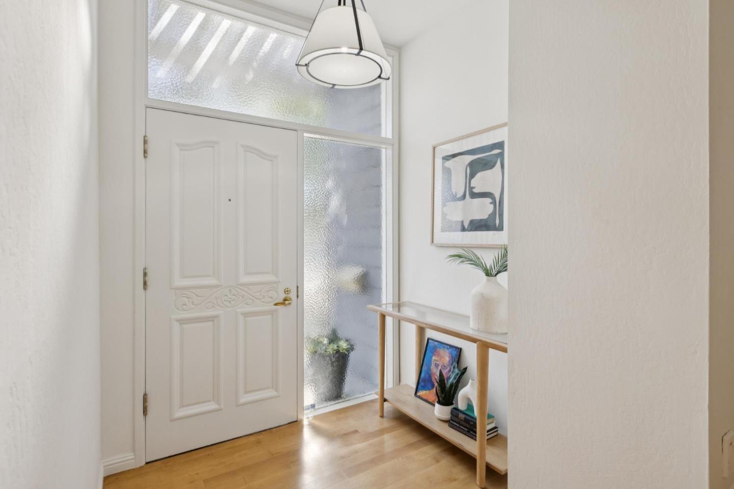 Furnished foyer with a paneled white front door, frosted-glass sidelights, and a light wood console table.