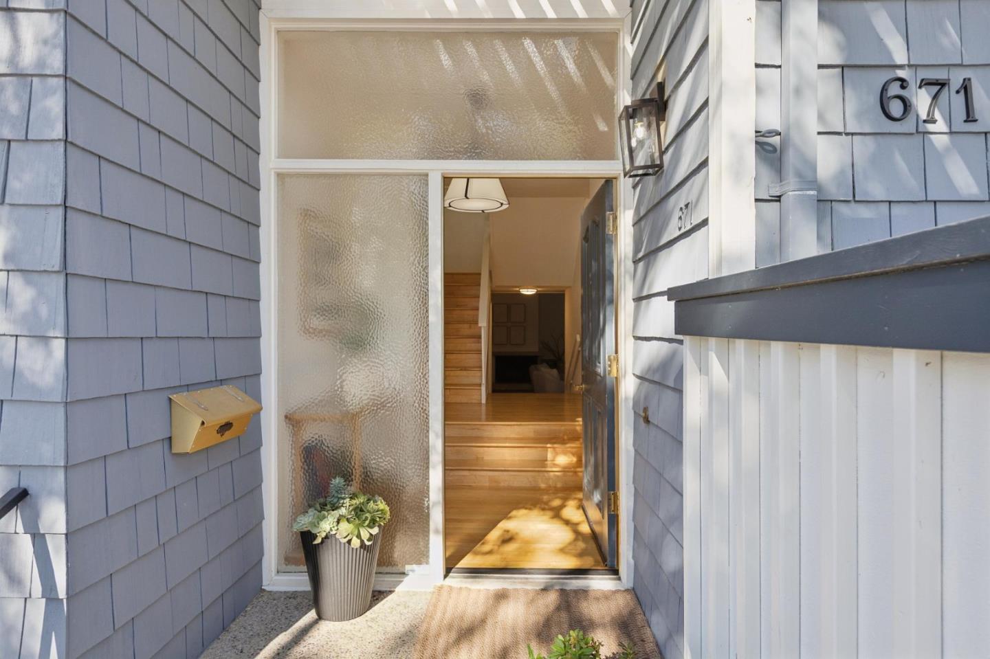 Home entrance with blue-gray shingle siding, open door, wood steps, and potted succulent.