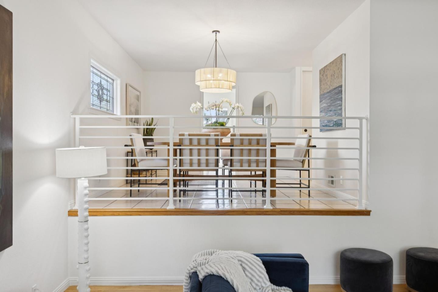 Raised dining area with a white railing, wooden table, pendant light, and stained-glass window.