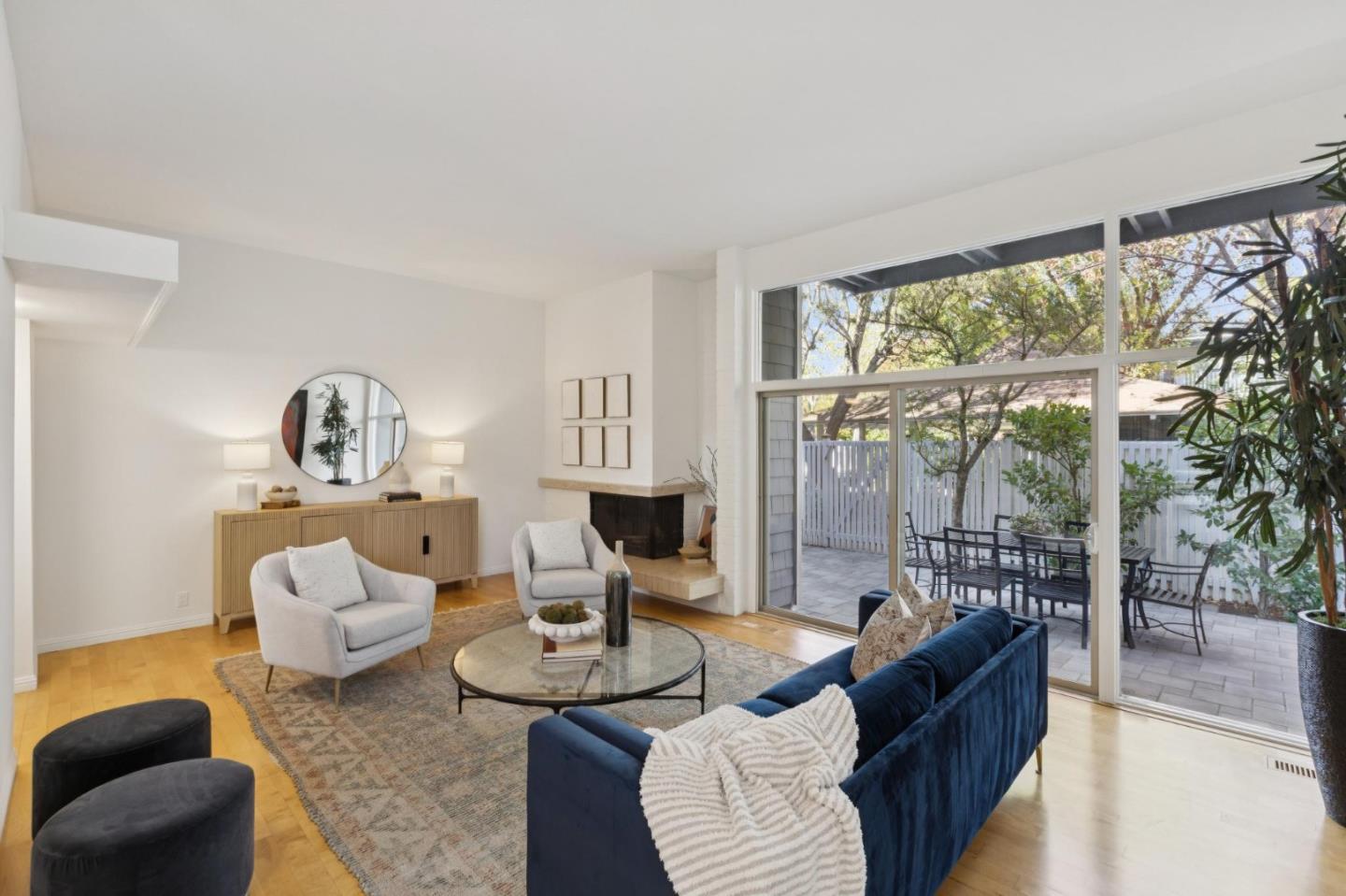 Living room with a blue sofa, fireplace, and large windows overlooking a fenced patio.