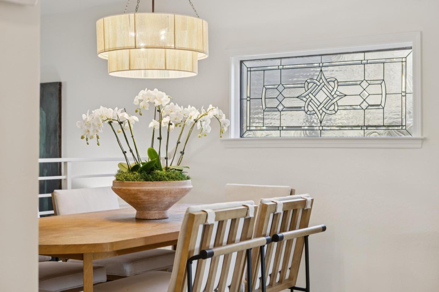 Dining room with a wooden table, white orchid centerpiece, and decorative stained-glass window.