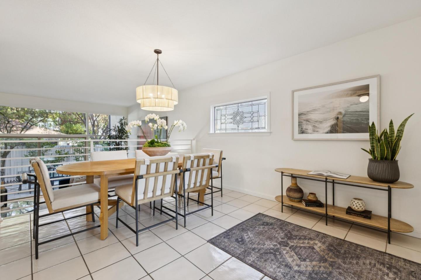 Dining room with a wooden table, large windows, stained-glass accent window, and tiled floor.