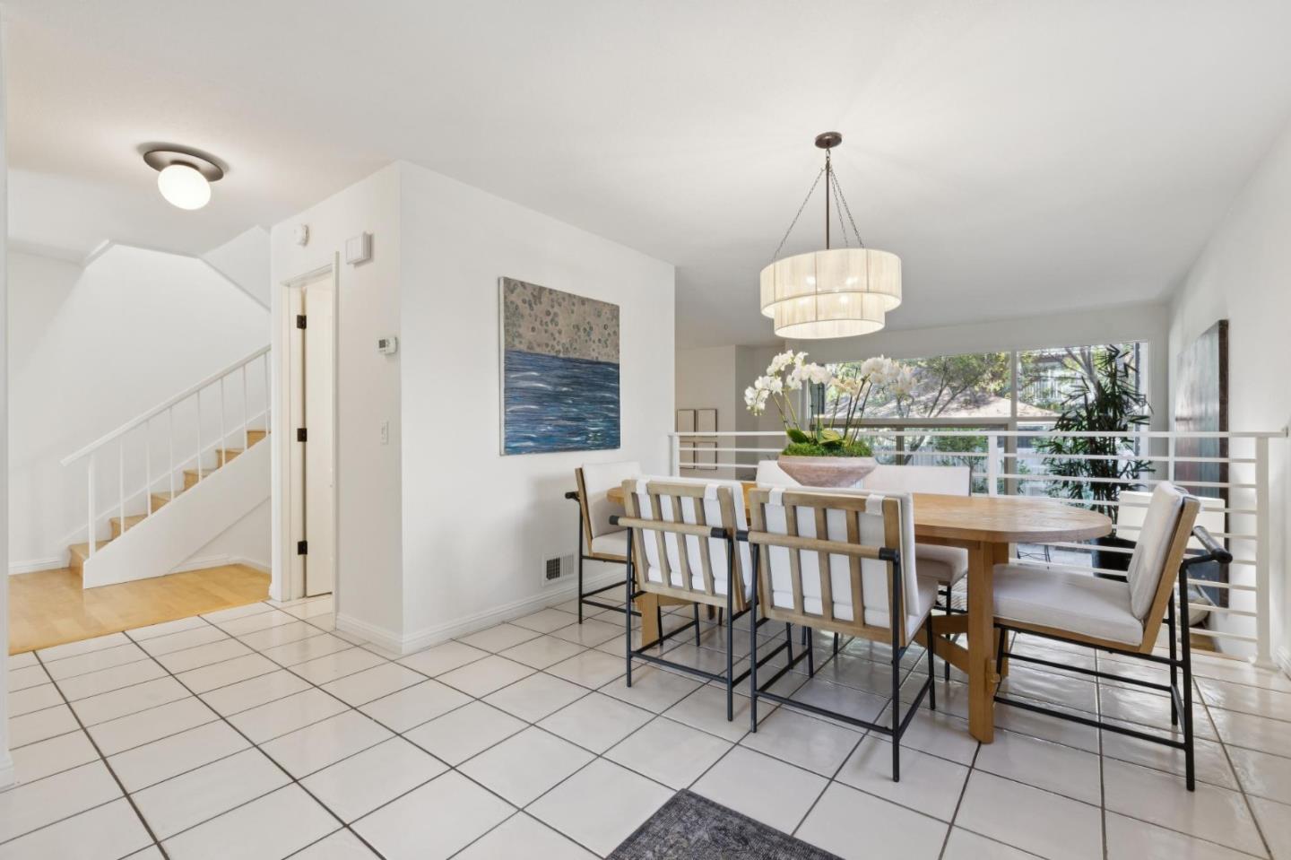 Dining area with a wooden table, pendant light, tiled floor, and staircase beside large windows.