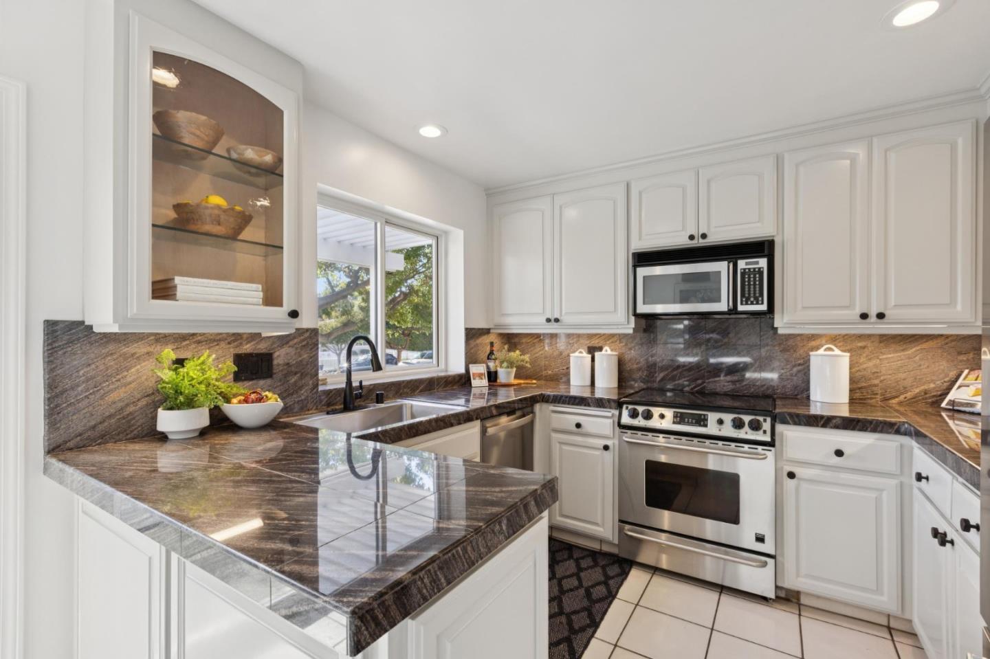 Kitchen with white cabinets, dark stone counters, stainless steel appliances, and a sink by the window.