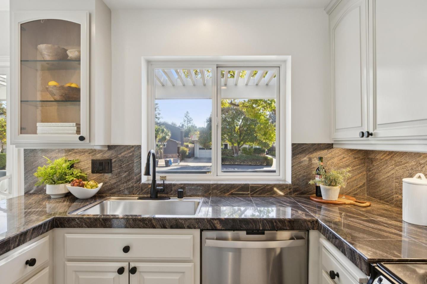 Kitchen with white cabinets, dark stone counters, and a window overlooking trees.