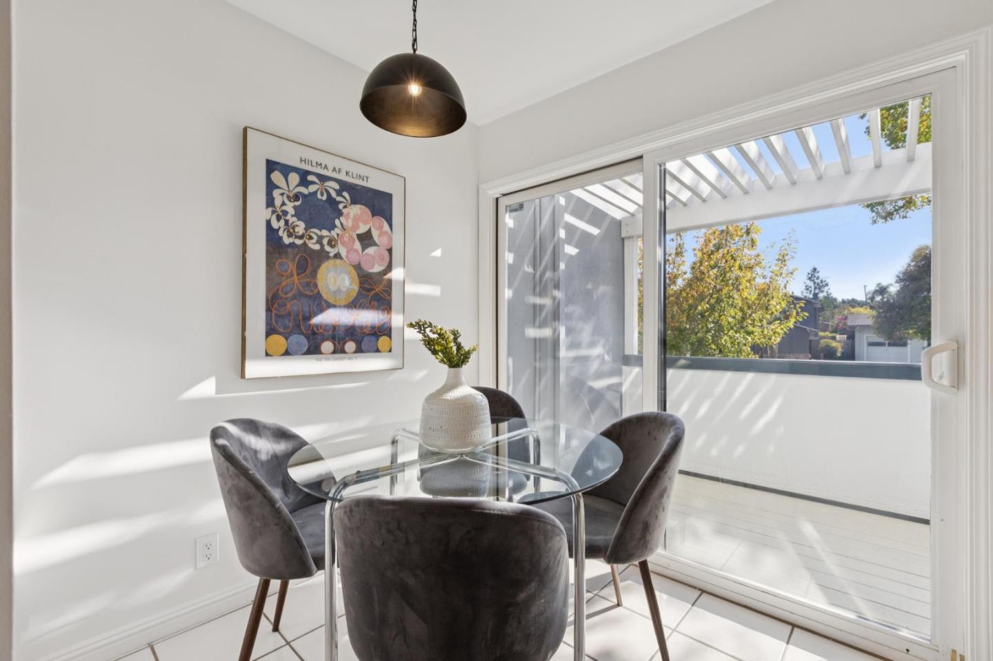 Dining area with a glass table and gray chairs beside sliding patio doors.