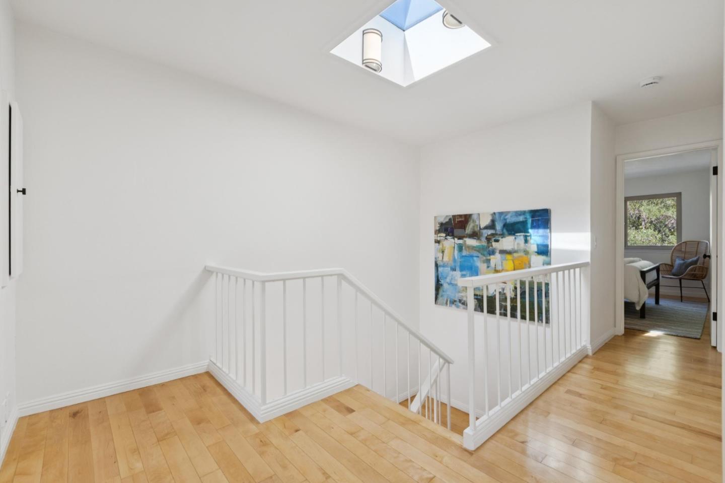 Bright upstairs landing with hardwood floors, white stair railings, and a skylight.