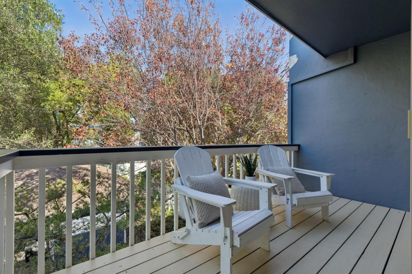 Covered balcony with two white Adirondack chairs overlooking leafy trees.